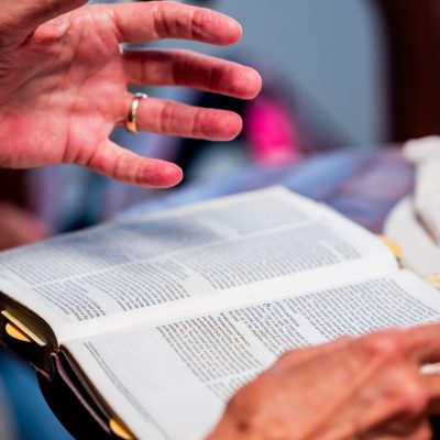 Close-up of hands engaged in Bible study at an indoor setting, promoting spiritual discussion.